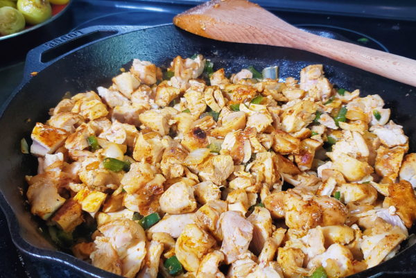View of cut chicken added to onions and peppers